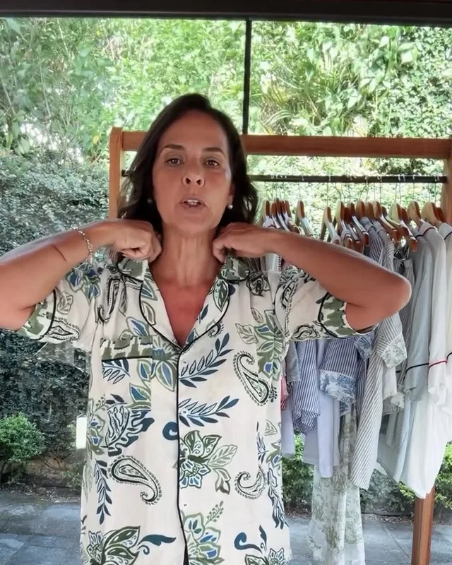 Márcia, dona da Dona Alice Comfy, mostrando um pijama de estampa de folhagem em frente à arara de peças
