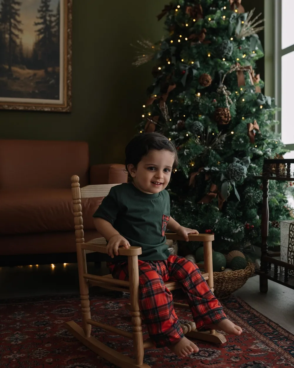 Menino de pijama xadrez numa cadeira de balanço ao lado da árvore de Natal