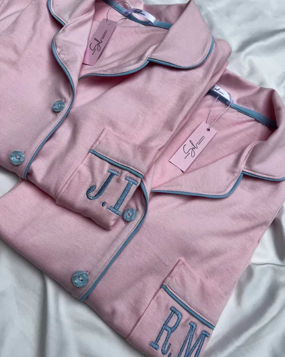 Pijama rosa com vivo azul, botões azuis e iniciais bordadas no bolso