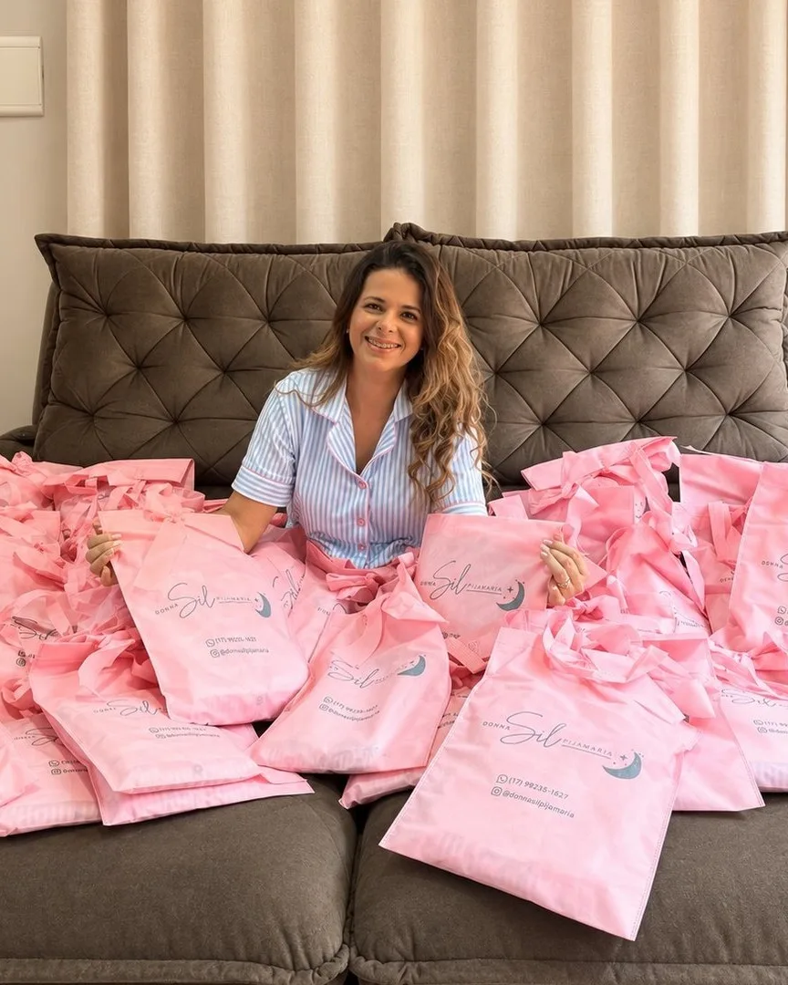 A Sil sentada no sofá, entre as ecobags rosa dos pedidos prontos