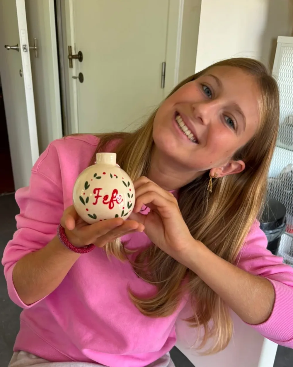 Menina sorrindo com uma bola de Natal de cerâmica com o nome Fefe pintado à mão