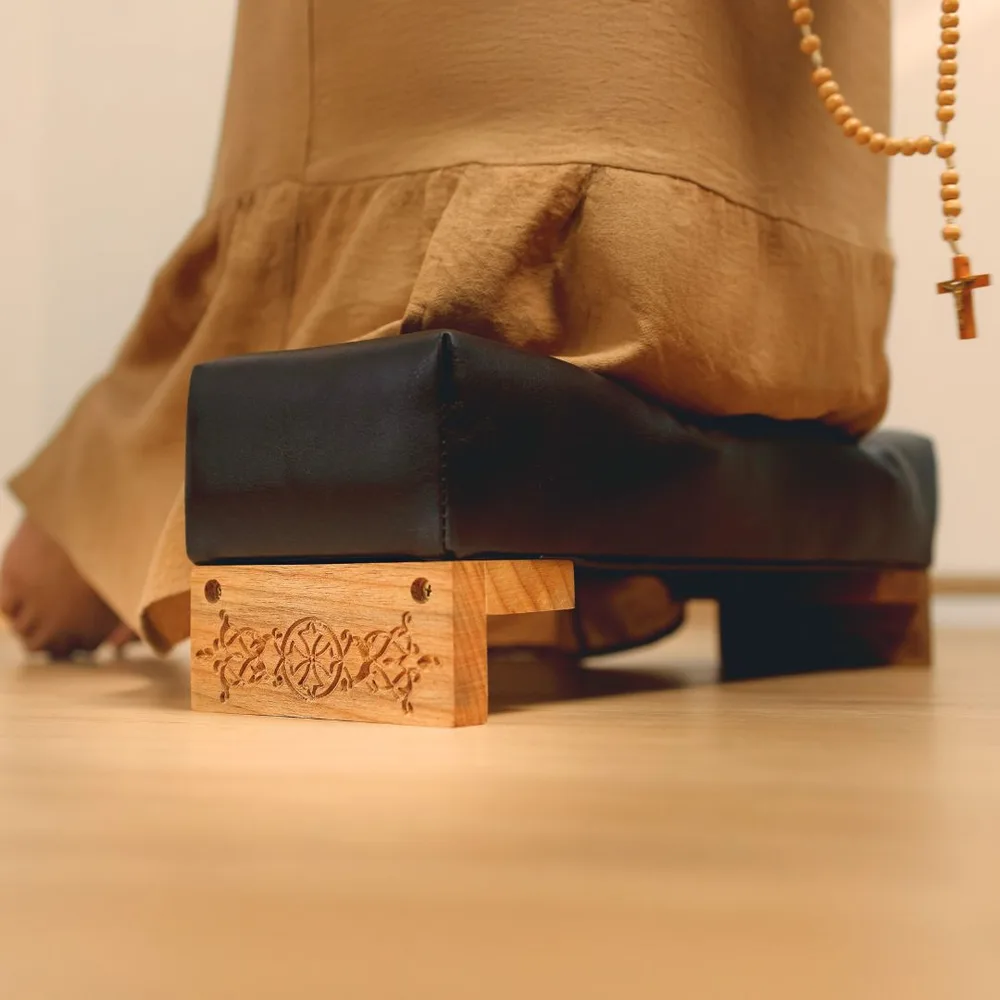 Pessoa ajoelhada no genuflexório estofado, com um terço nas mãos